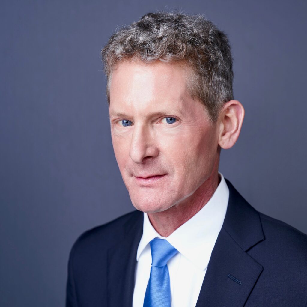 Close-up of the attorney Paul W. Palley wearing a navy suit, white shirt, and blue tie against a blue-gray backdrop, showing facial features from the nose up to the eyes.